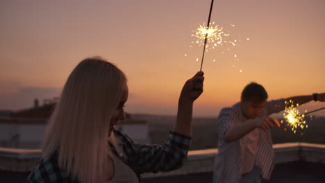 Girl-raises-their-hands-up-and-jump-on-the-roof-with-big-bengal-light-in-their-hands.-It's-a-crazy-party-at-night.